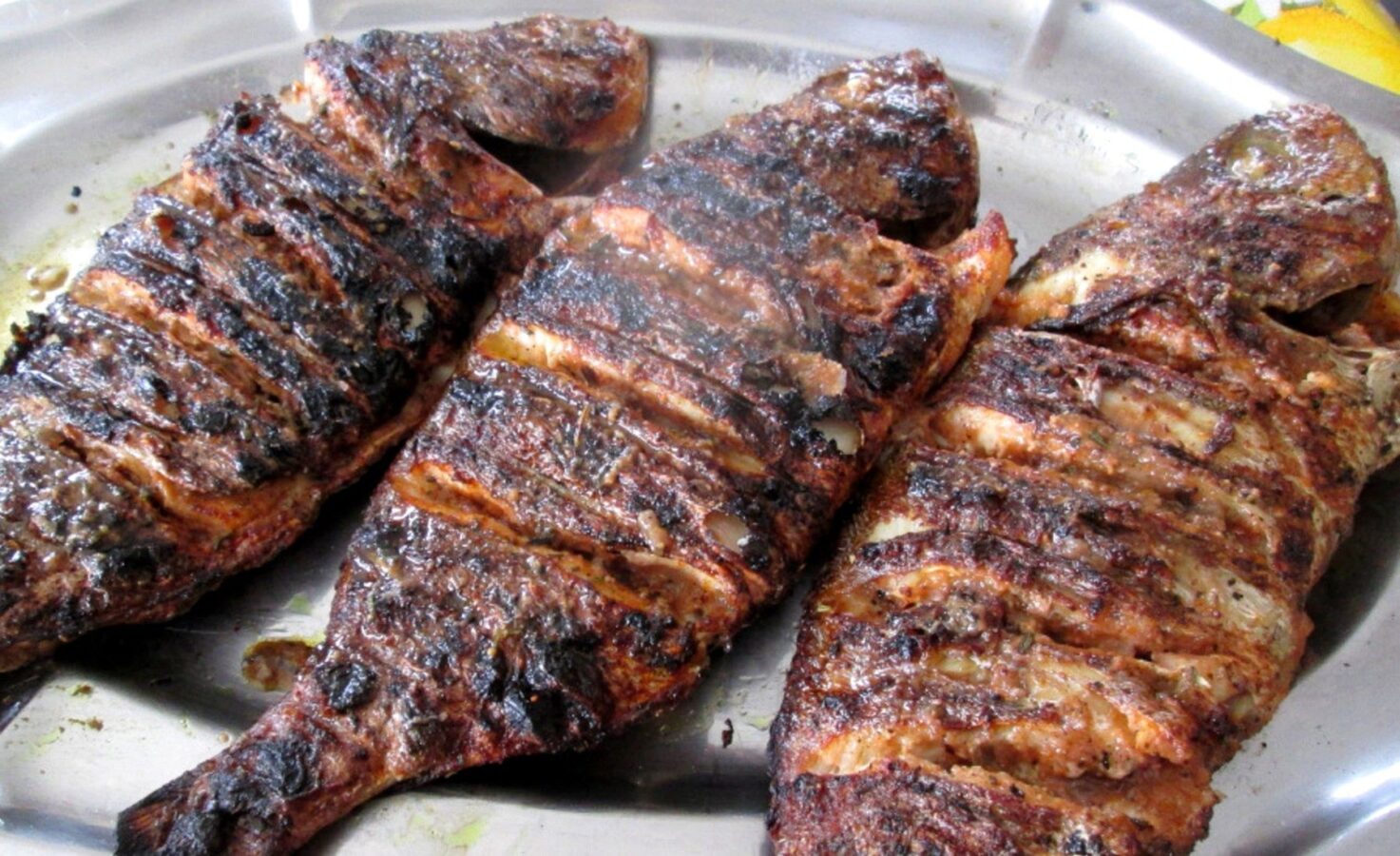 Trois poissons grillés servis sur un plateau, typiques de la cuisine sénégalaise.
