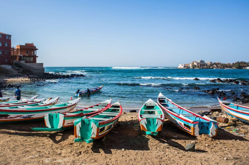 Pirogues colorées alignées sur la plage avec vue sur l'océan Atlantique à Dakar, Sénégal.