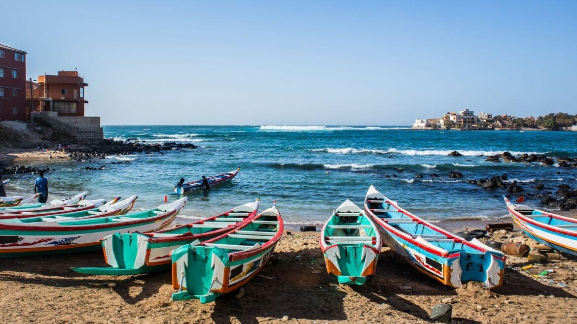 Pirogues colorées alignées sur la plage avec vue sur l'océan Atlantique à Dakar, Sénégal.