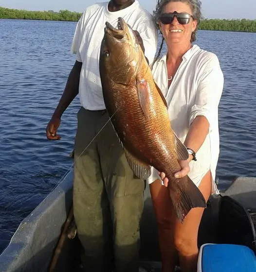 Cliente et guide tenant une carpe rouge sur une coque ouverte dans le delta du Sine et Saloum