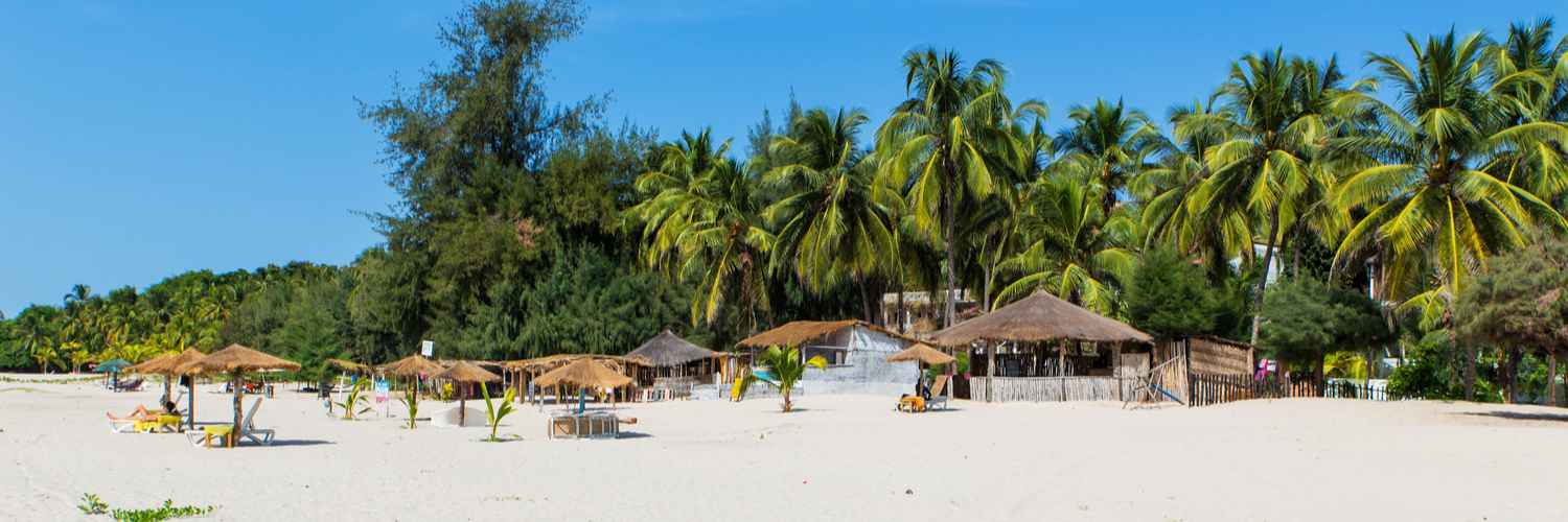 Plage du Cap Skirring en Casamance, avec des parasols en paille et des cocotiers sous un ciel bleu.