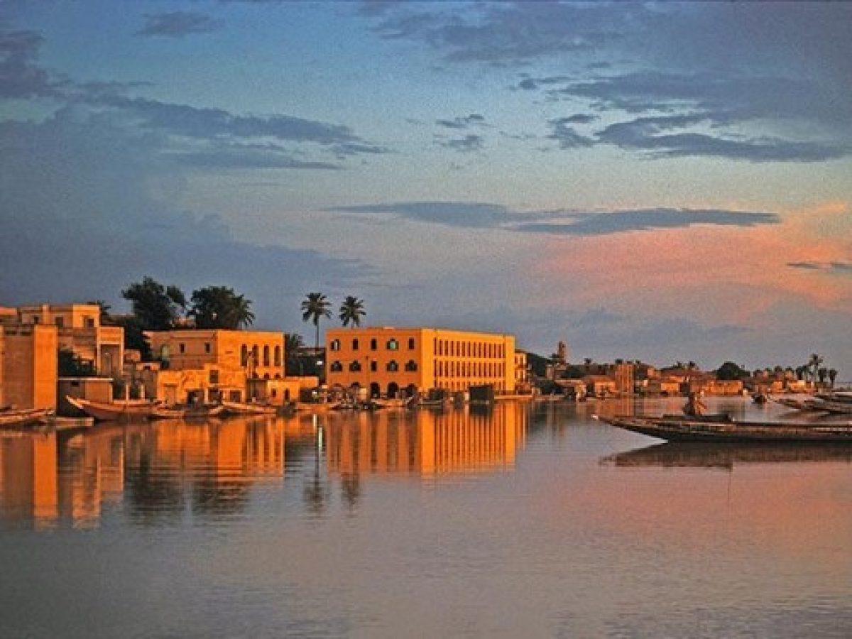 Coucher de soleil à Saint-Louis du Sénégal, avec ses bâtiments coloniaux reflétés sur le fleuve.