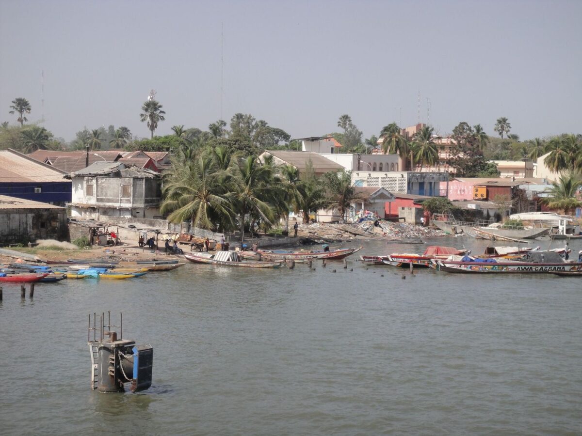 Vue du port de Ziguinchor en Casamance, avec des pirogues traditionnelles et des bâtiments en bord de rivière.